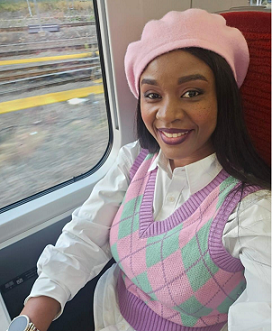 Girl wearing a pink sweatshirt and white shirt with a pink hat, sat next to the window on a train